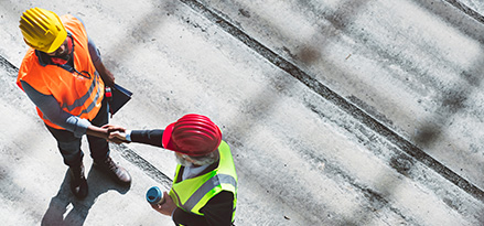 Photo taken from above of two workers in high visibility jackets and hard hats shaking hands with one another