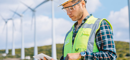 Engineer stands in front of wind turbines working on his tablet device