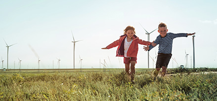 Two children playing in a field with wind turbines behind them